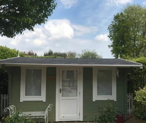 Green garden building with white door and window frames.